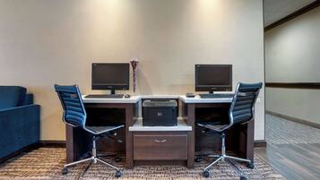 A hotel room with two desks, each with a computer and chair, a printer, and a small vase with flowers.