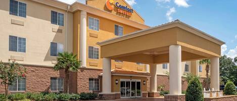 A Comfort Suites hotel with a covered entrance, multiple windows, and a landscaped entrance area.