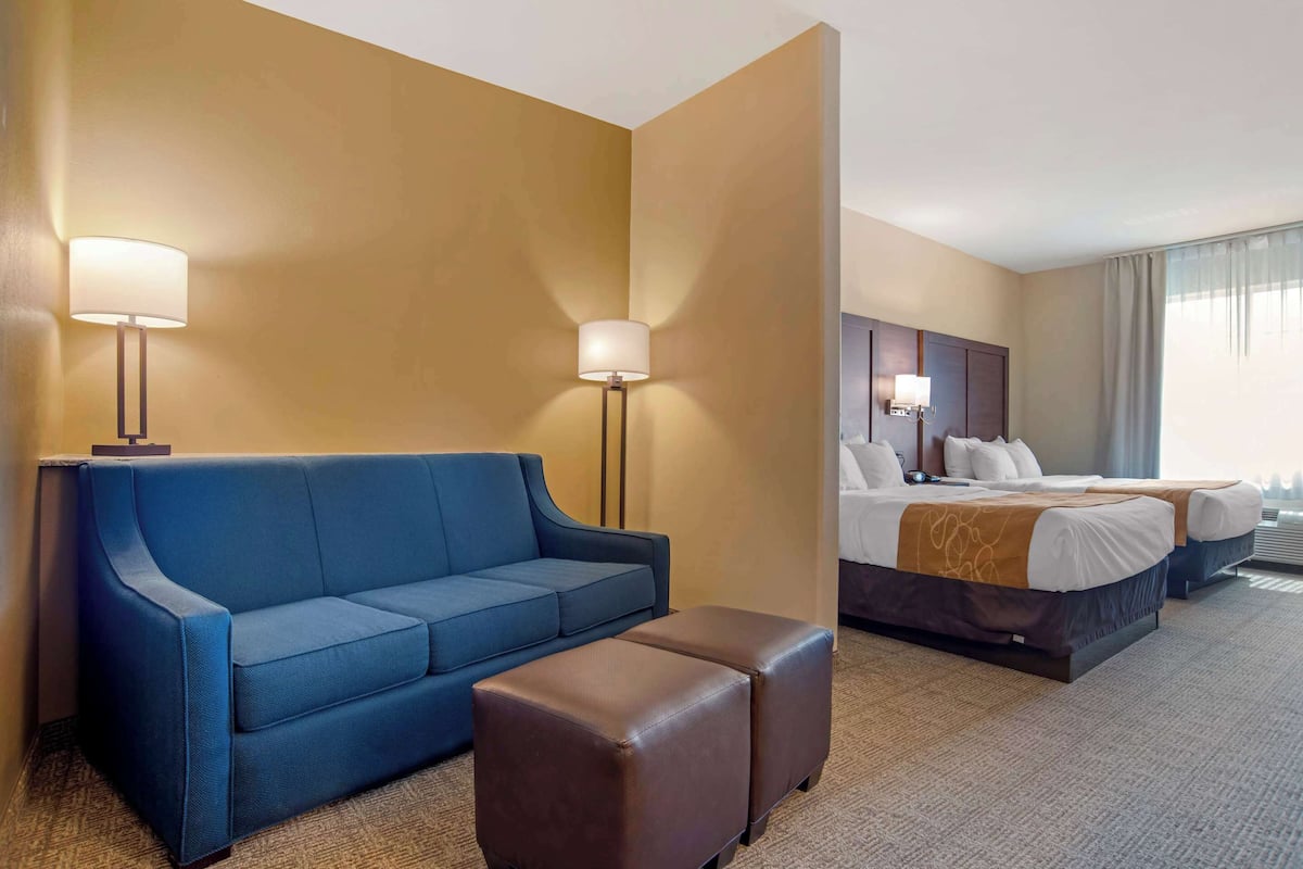 Une chambre d’hôtel avec un canapé bleu, un pouf marron, un lit avec deux oreillers et une table de chevet.