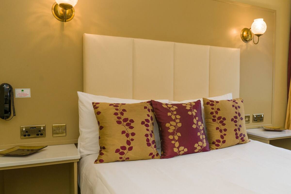 A hotel room with a bed, bedside tables, a phone, and a window with curtains.