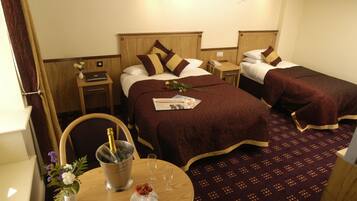 A hotel room with two beds, a small table with a bottle of champagne, a vase with flowers, and a newspaper.