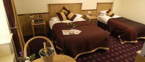 A hotel room with two beds, a small table with a bottle of champagne, a vase with flowers, and a newspaper.