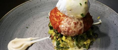 Un plat composé d’un œuf poché, d’un aliment pané et de légumes verts, servi dans une assiette en céramique à motifs.