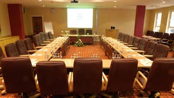 Un salón de conferencias con una larga mesa, varias sillas y una pantalla para proyector.