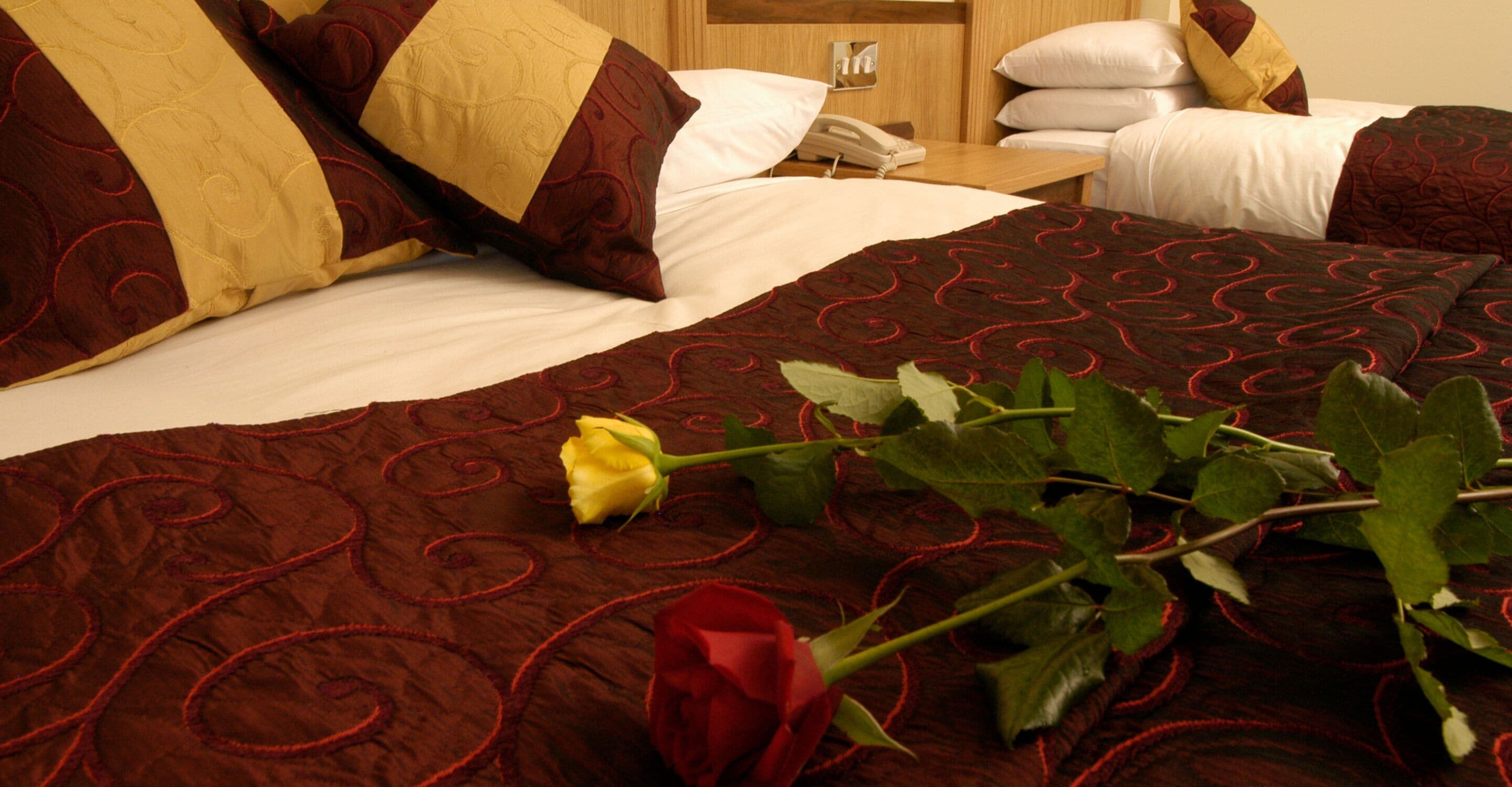 Una cama bien hecha con una rosa roja y una rosa amarilla sobre una colcha estampada.