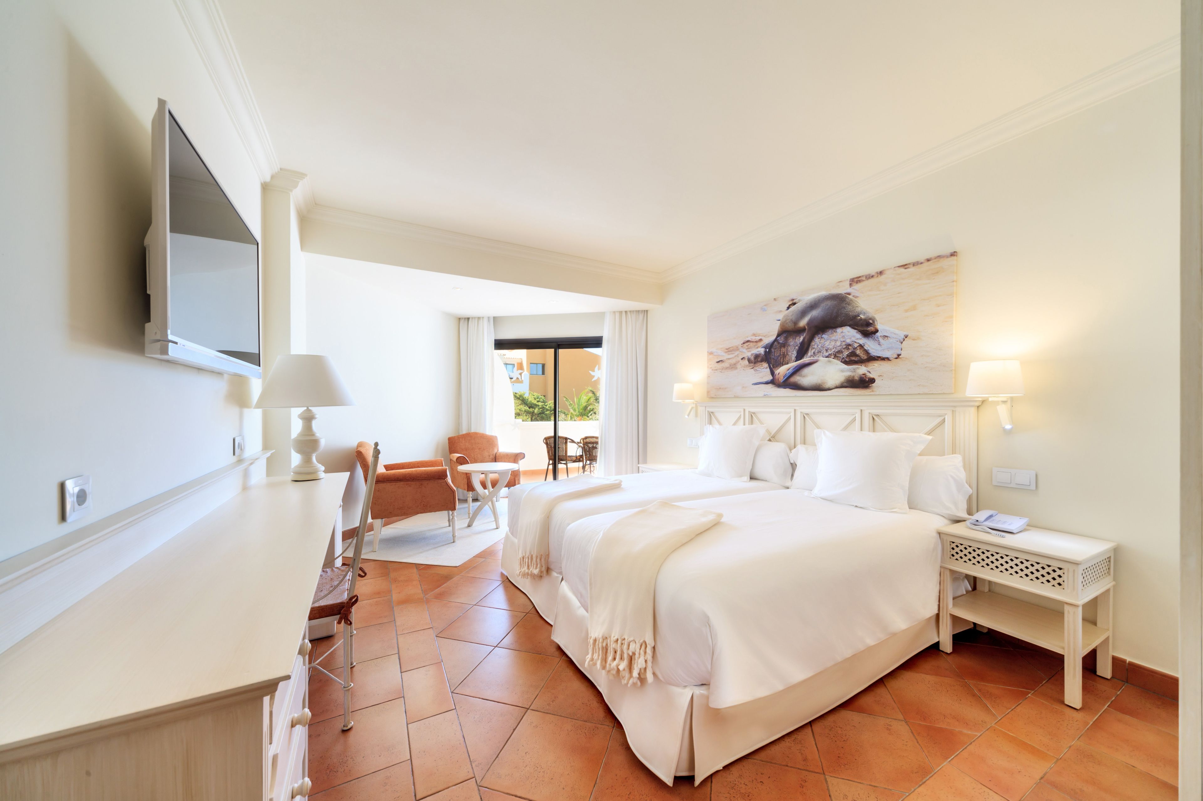 Ein Hotelzimmer mit Bett, Schreibtisch, Stuhl, Fernseher und einem Bild an der Wand.