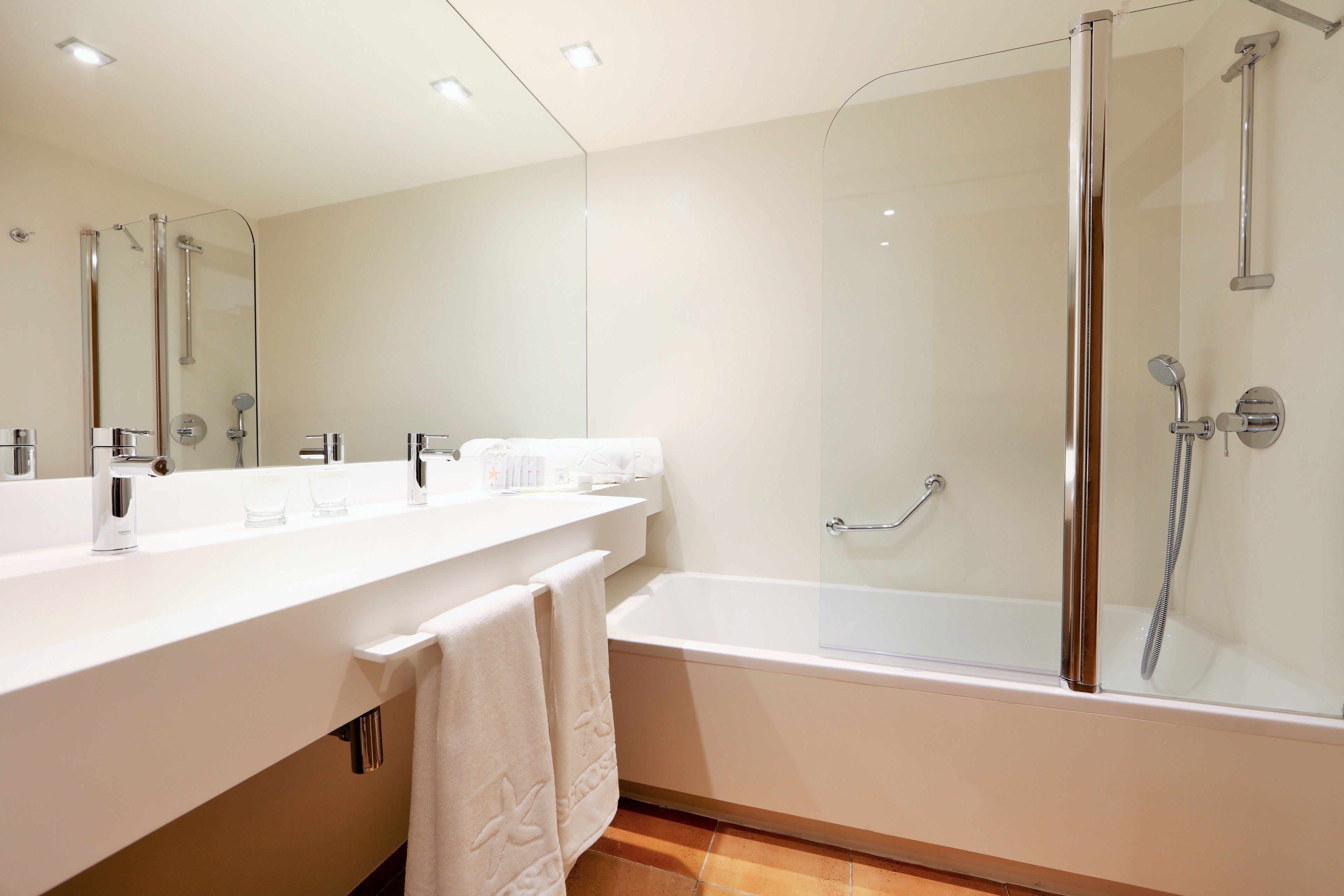 A modern bathroom with a large mirror, a white countertop, a bathtub, and a glass-enclosed shower area.