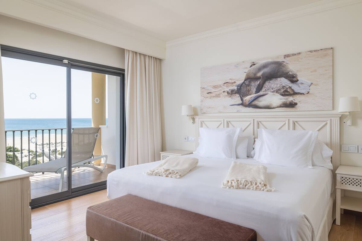 Habitación de hotel con una cama grande, un balcón con una silla y un cuadro de lobos marinos en la pared.