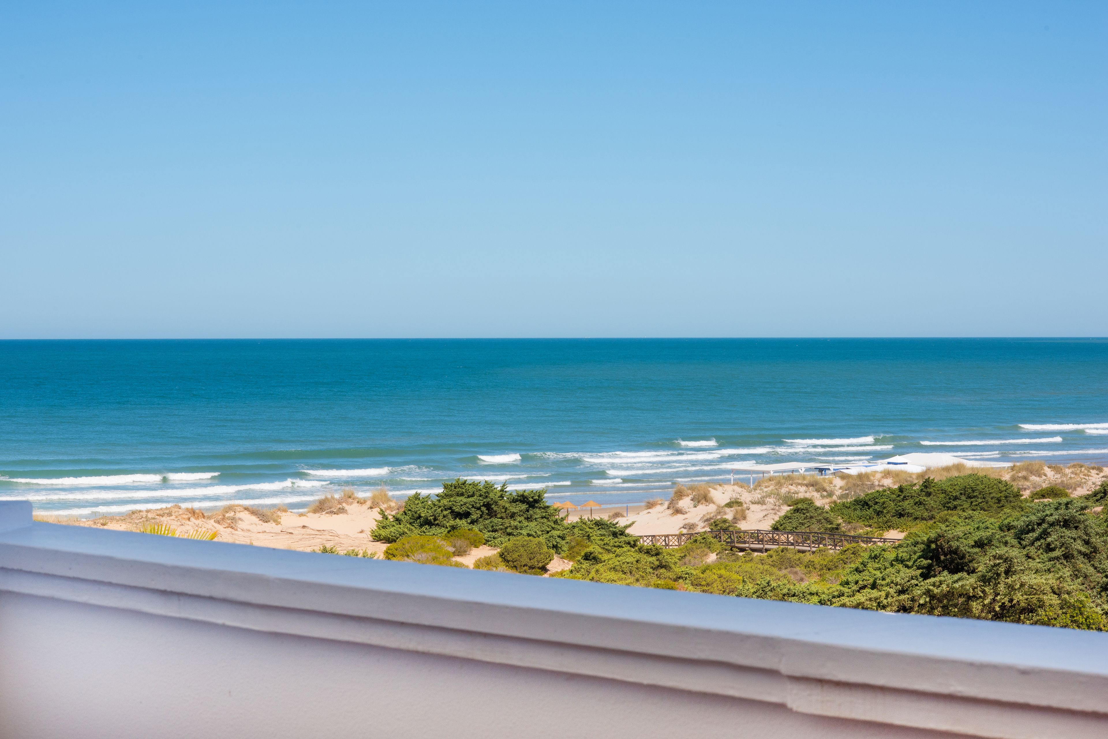 Une vue sur la côte, depuis un balcon donnant sur l’océan, avec une plage de sable et une végétation luxuriante.