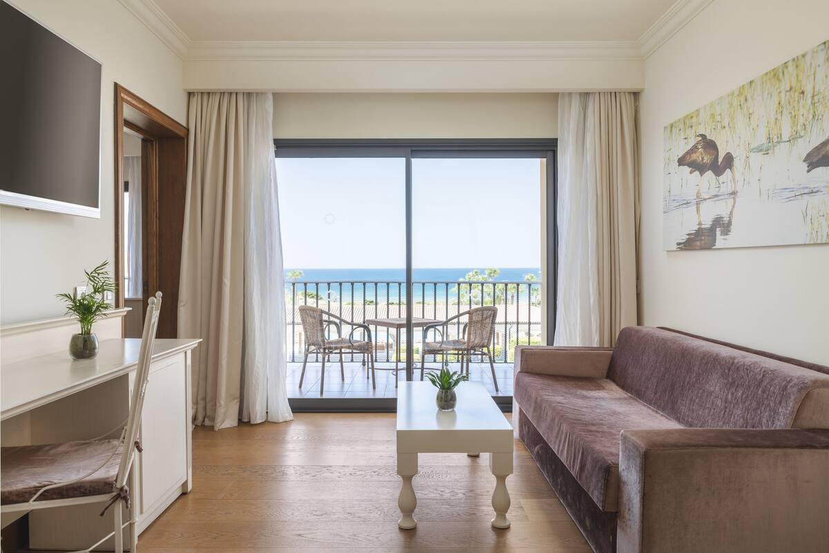 Una sala de estar con sofá, mesa de centro, televisor y balcón con vista al mar.