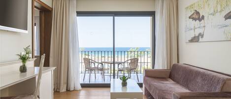 Ein Wohnzimmer mit einer Couch, einem Couchtisch, einem Fernseher und einem Balkon mit Meerblick.
