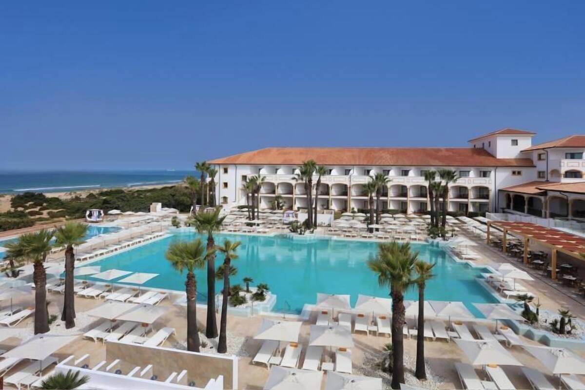 Un resort con una piscina grande, varios balcones y vista a la playa.