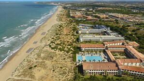 Vista aérea de un complejo turístico costero con playa, piscina y varios edificios de hotel.