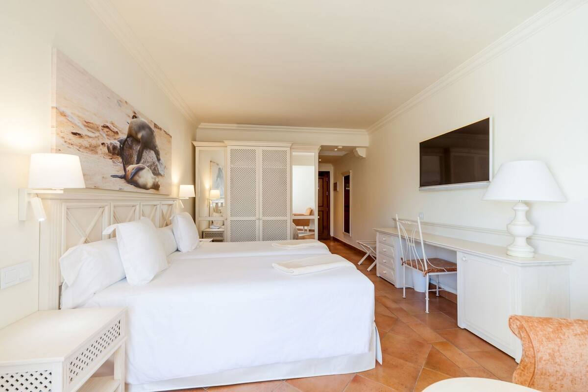 Habitación de hotel con una cama grande, un escritorio, una silla, un televisor y un cuadro en la pared.