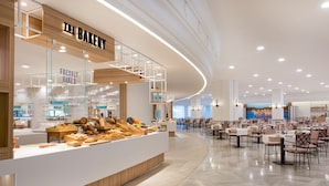Mostrador de panadería con diversas opciones de productos horneados y una zona de estar con mesas y sillas.