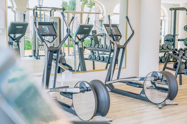 Un gimnasio con máquinas de cardio, equipo de levantamiento de pesas y mancuernas.