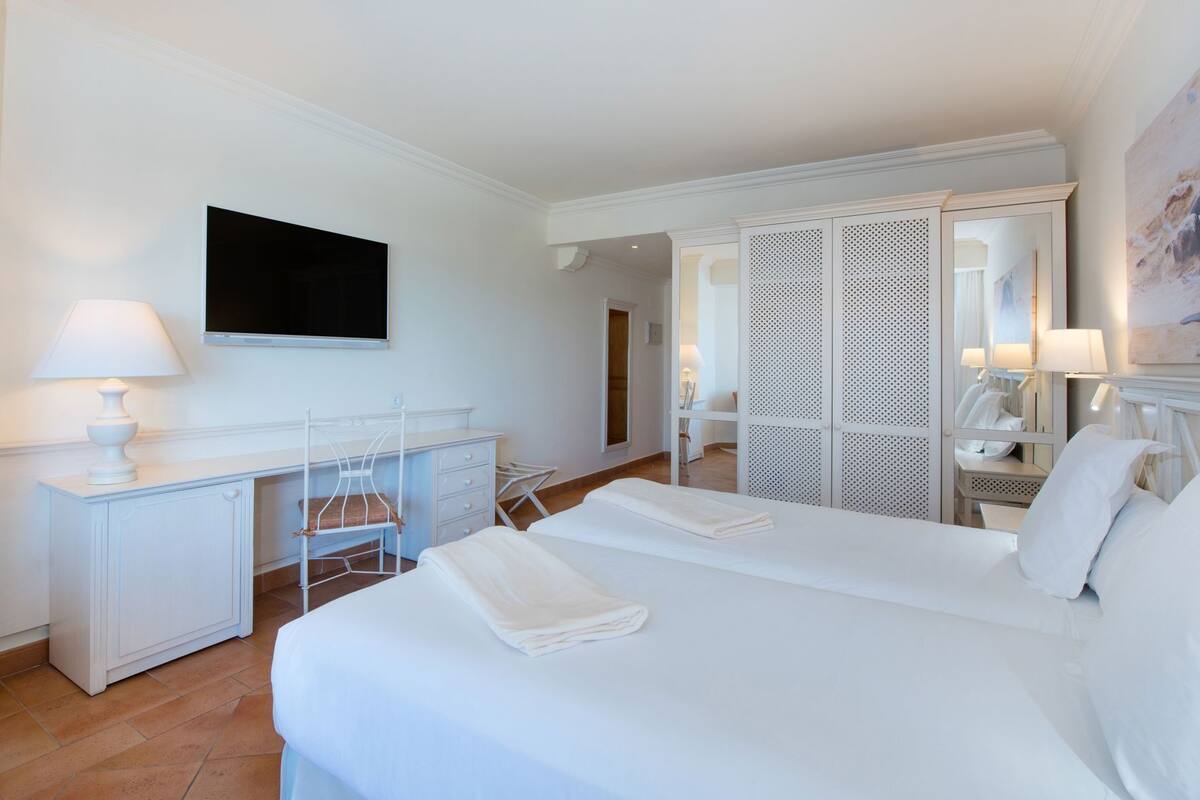 Una habitación de hotel con cama, escritorio, silla, televisor y armario.