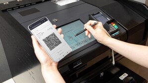 A person using a smartphone and a pen to interact with a printer, possibly for printing a receipt or document.
