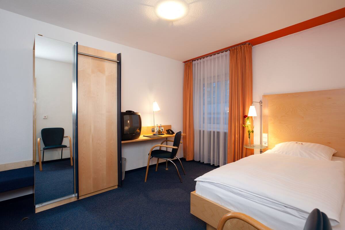 Une chambre d’hôtel comprenant un lit, un bureau avec une chaise, une télévision et un miroir.