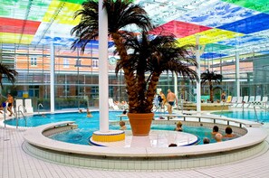 An indoor swimming pool with a central palm tree, surrounded by lounge chairs and a tiled floor. - PARKHOTEL Helene (Bad Elster)