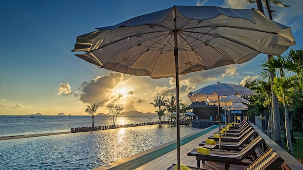 A poolside area with lounge chairs and umbrellas, overlooking a body of water with a sunset in the background. - Islanda Hideaway Resort (Krabi)