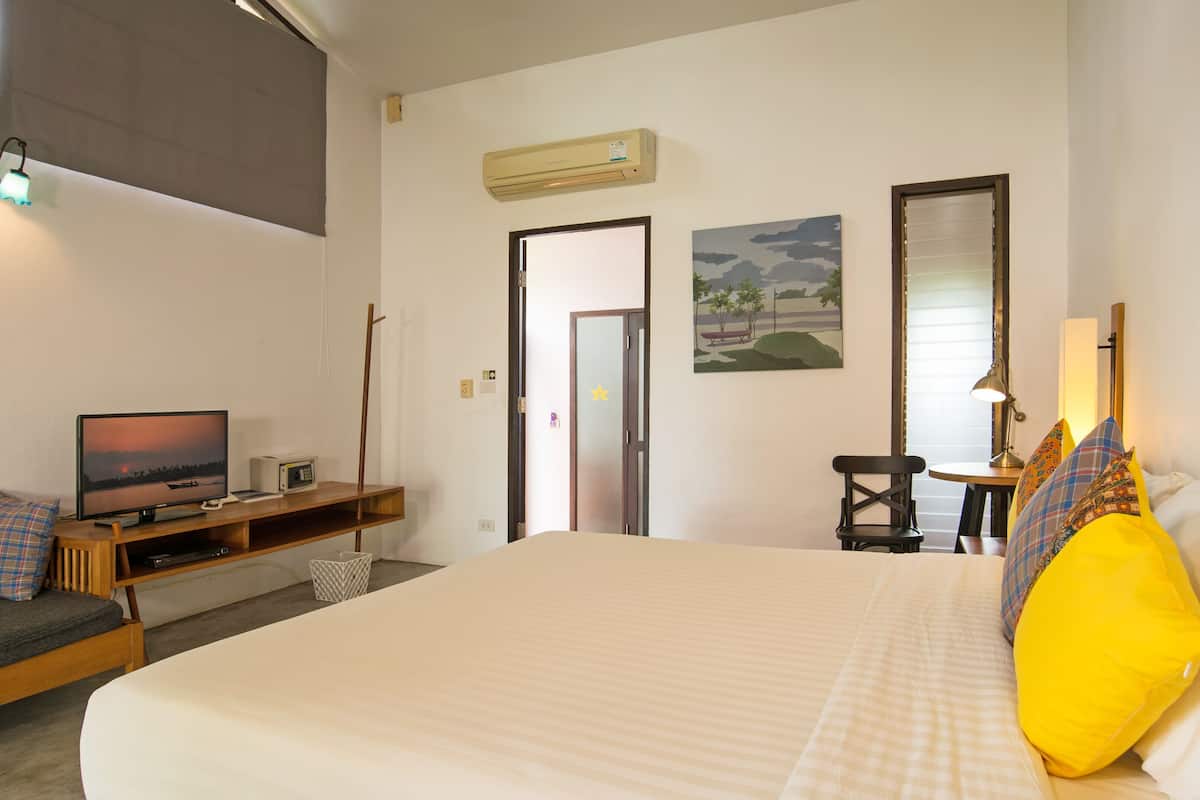 Habitación de hotel con una cama, un televisor sobre un soporte de madera, un escritorio con una silla y un cuadro en la pared.