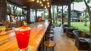 A bar area with a red drink, wooden furniture, and a view of the outdoors. - Islanda Hideaway Resort (Krabi)