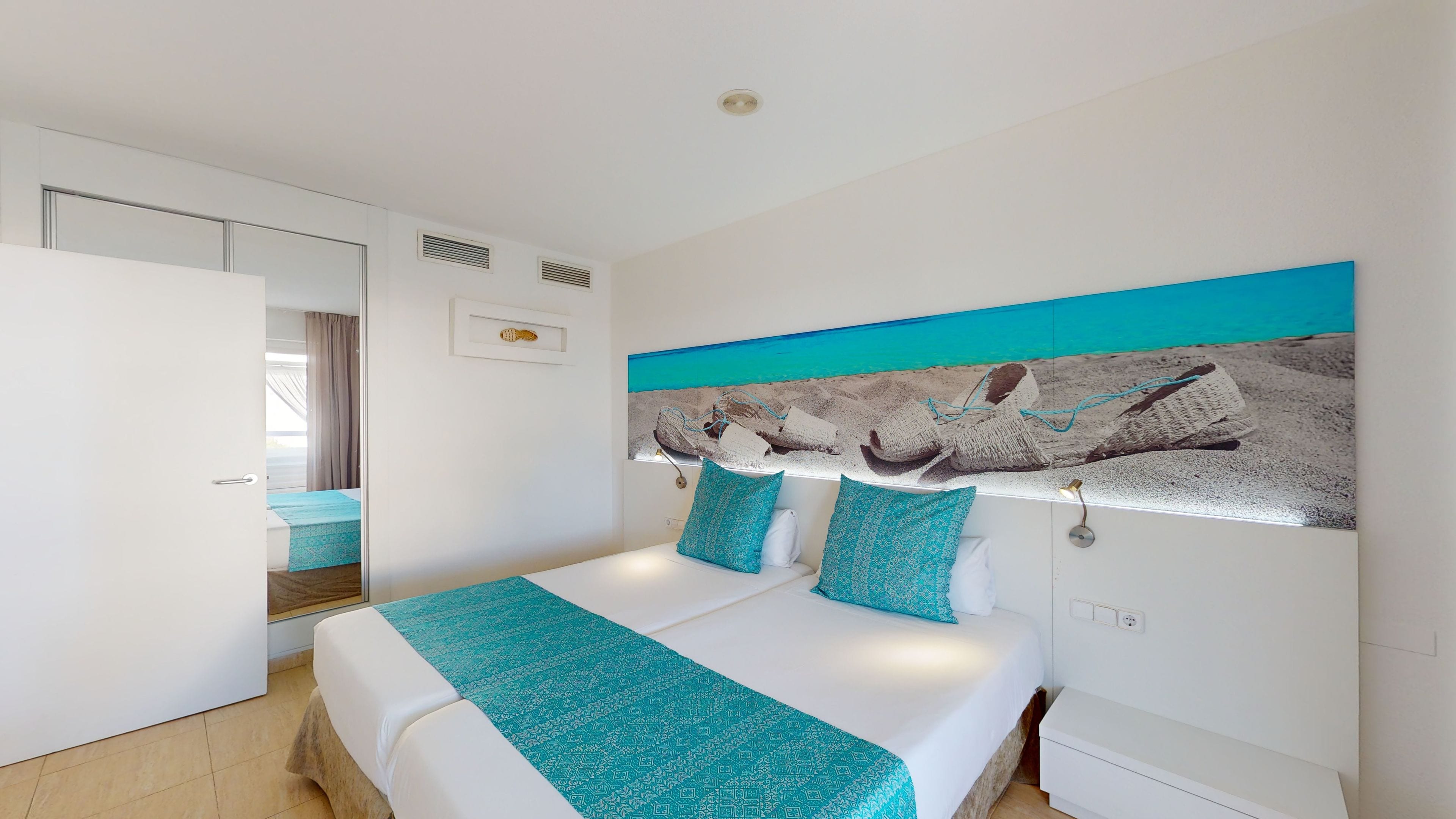 Ein modernes Schlafzimmer mit einem großen Bett, einem Kopfteil mit strukturierter Gestaltung und Blick auf einen Strand durch das Fenster.
