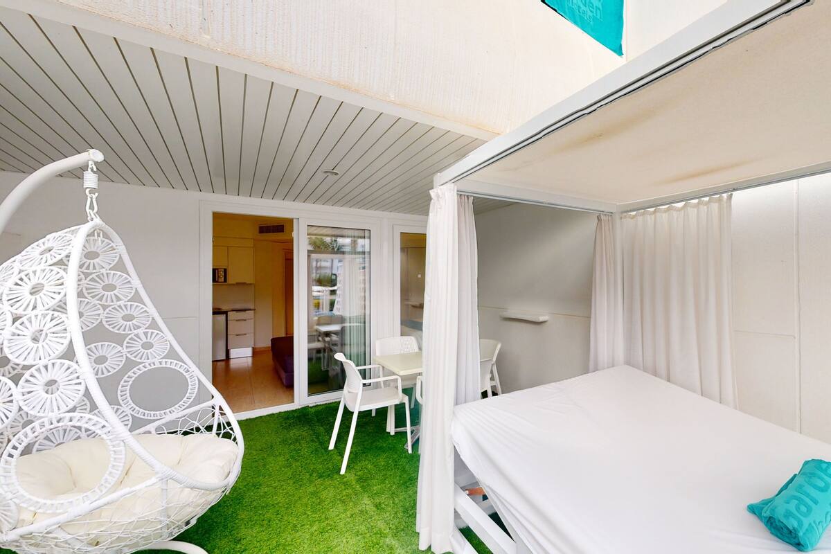 Una habitación pequeña con cama, una silla colgante y una mesita.