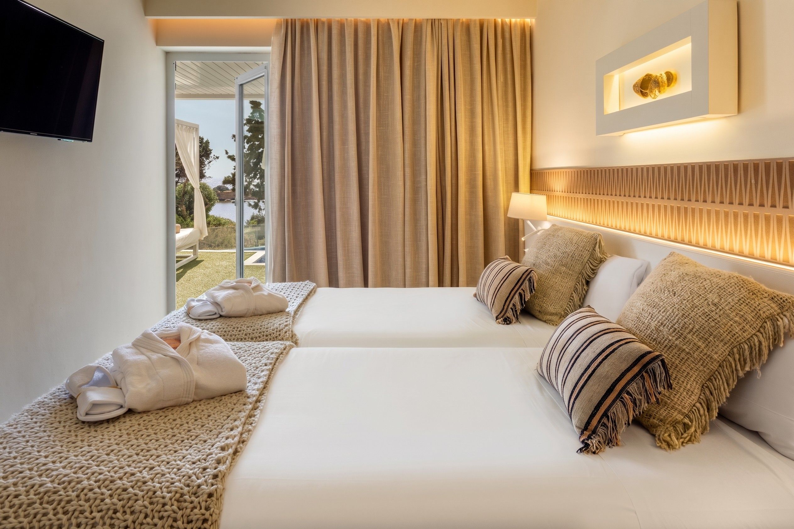 A hotel room with a bed, a TV, a window with curtains, and a view of the outdoors.