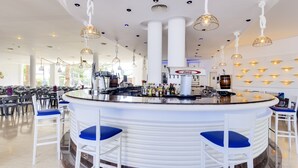 A modern bar area with a central counter, white bar stools, and hanging pendant lights. - Aparthotel Tropic Garden (Santa Eulalia del Rio)