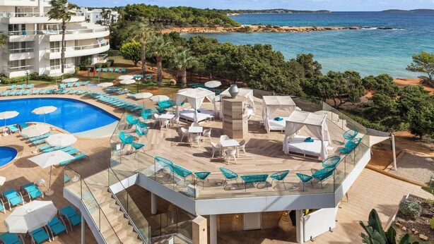 A resort with a pool, outdoor seating, and a view of the sea. - Aparthotel Tropic Garden (Santa Eulalia del Rio)
