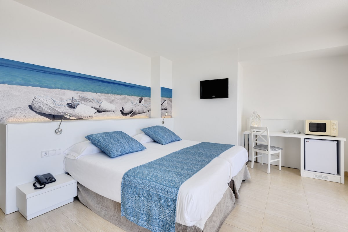 Un dormitorio con cama, escritorio, televisor y un refrigerador pequeño.