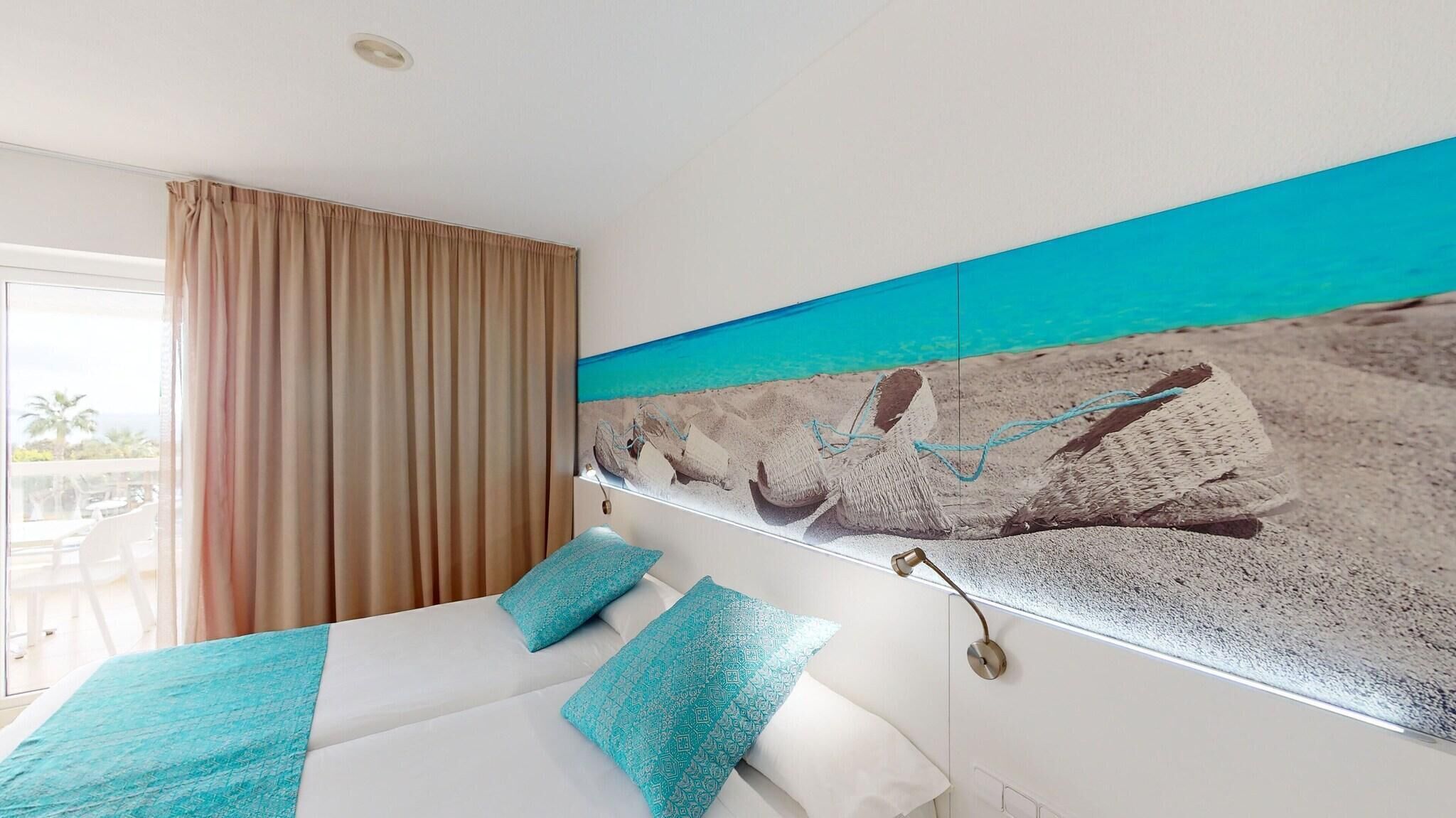 A hotel room with a bed, a view of the beach, and a balcony with a table and chairs.