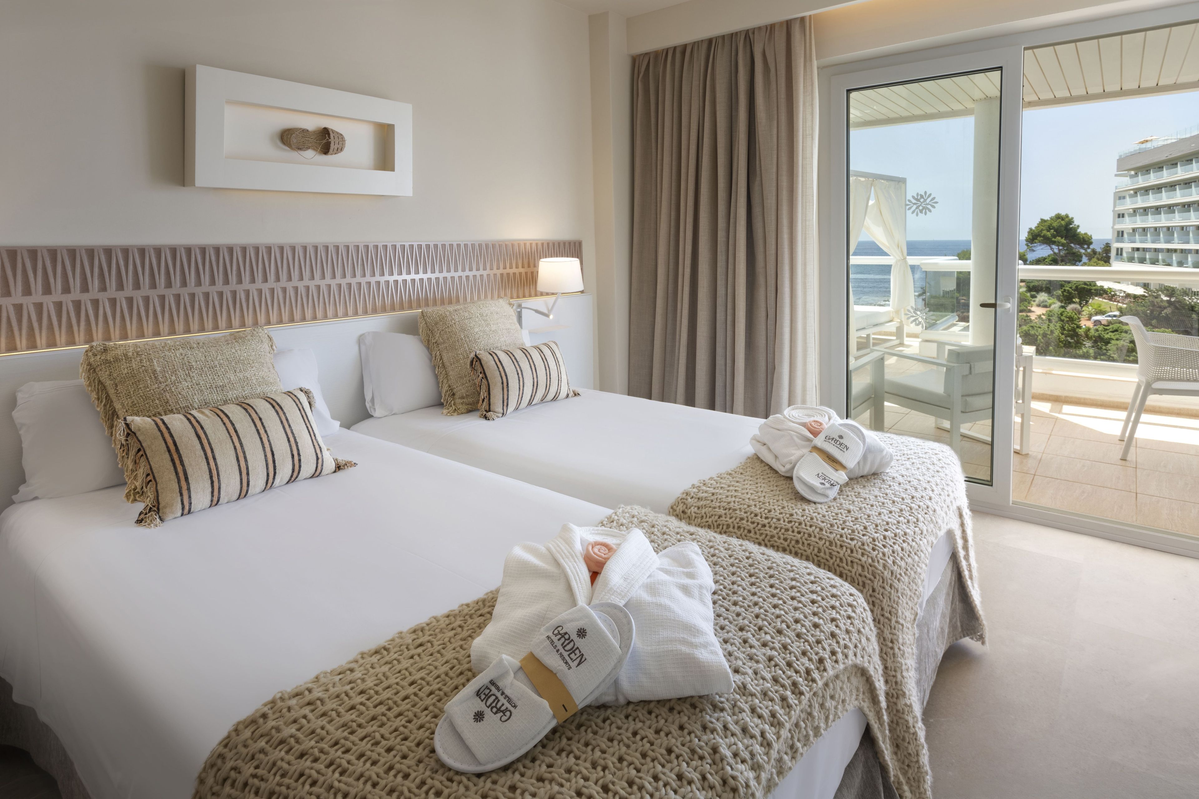 Een hotelkamer met twee bedden, uitzicht op zee en een balkon met een stoel.