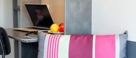 Un dormitorio con cama, escritorio con ordenador portátil y estante con libros y una caja.