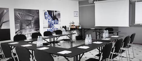 A conference room with tables, chairs, a projector, and a screen.