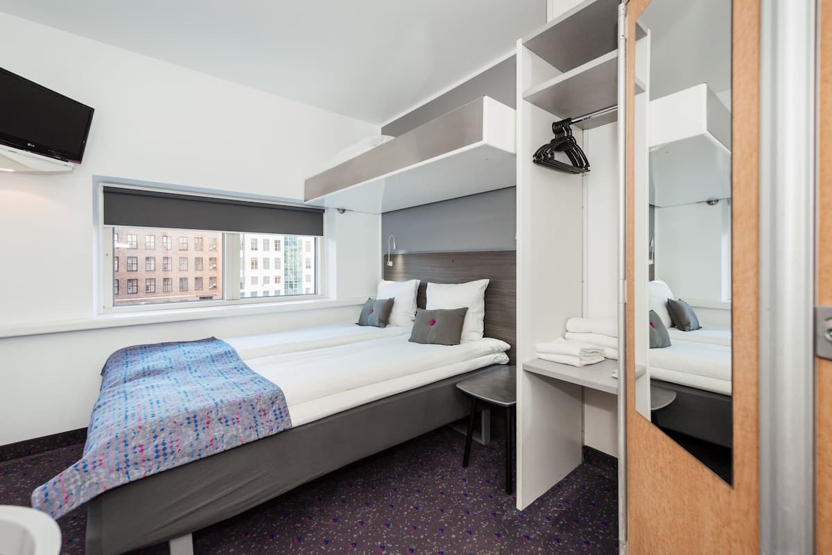 Een kleine hotelkamer met een bed, een tafeltje, een spiegel en een raam met uitzicht op de stad.