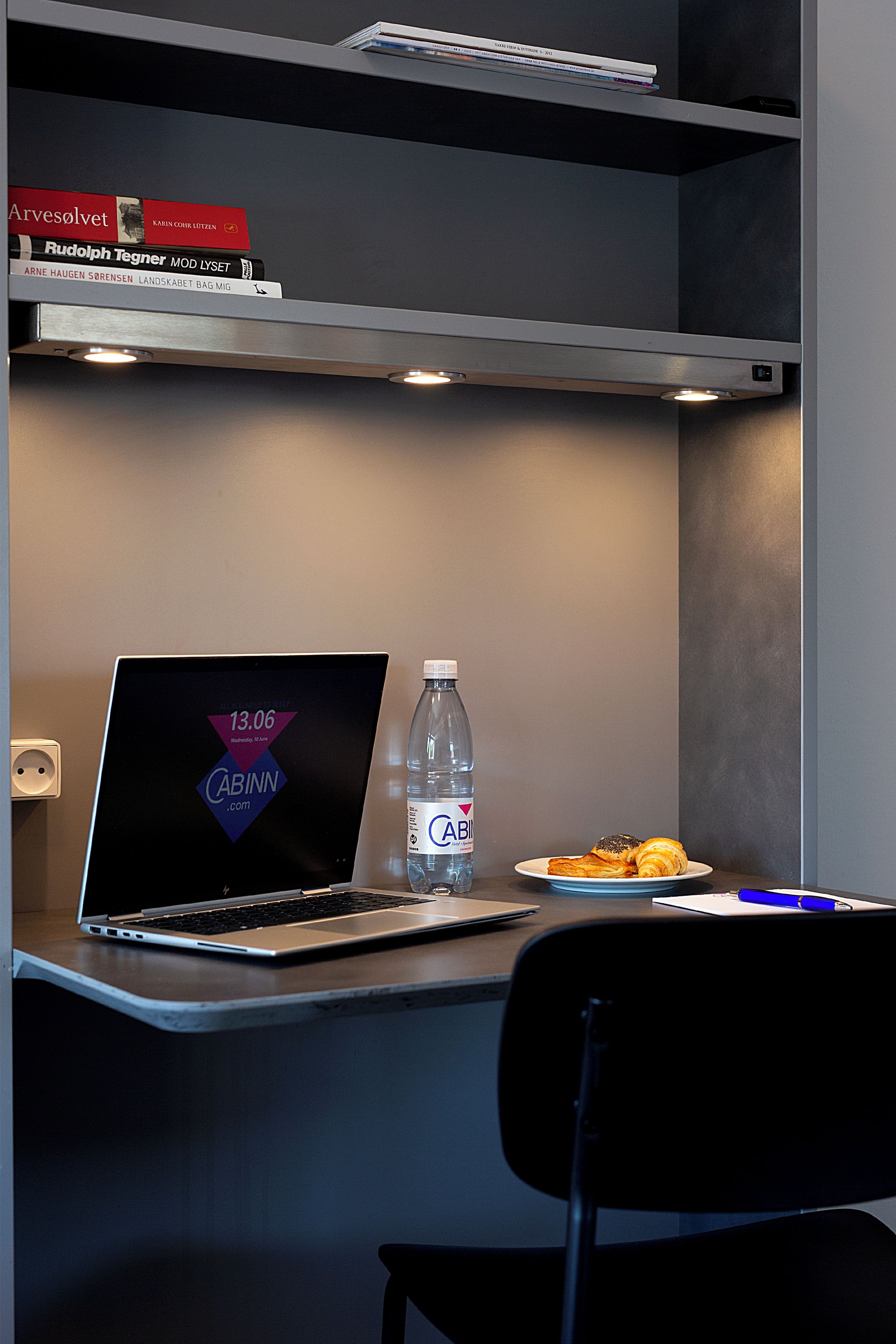 Un espace de travail moderne avec un ordinateur portable, une bouteille d’eau et une assiette de nourriture.
