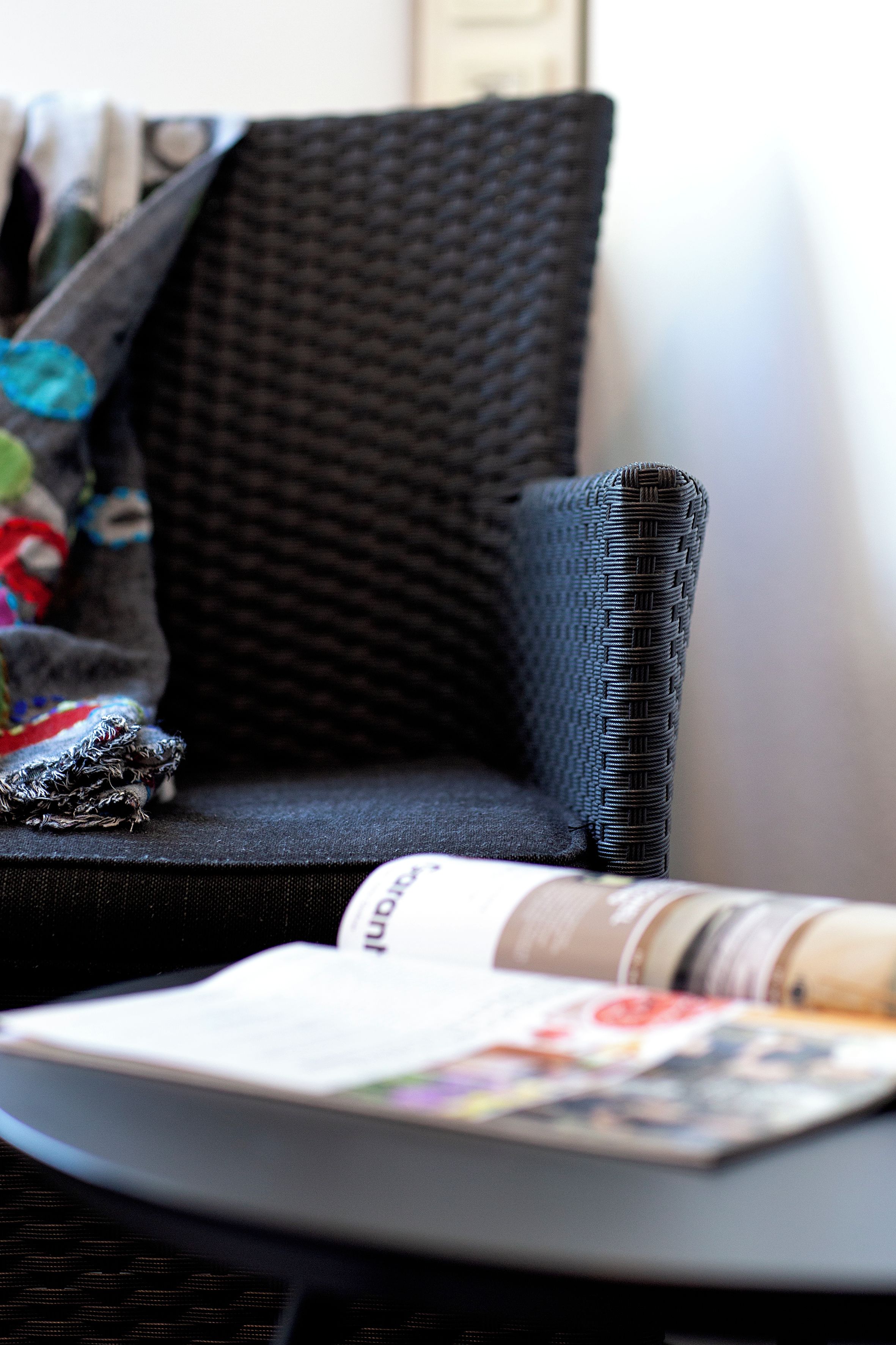 A close-up of a magazine on a table with a black woven chair and a cushion.