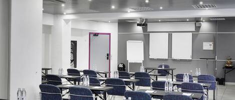 A conference room with tables, chairs, and a projector screen.