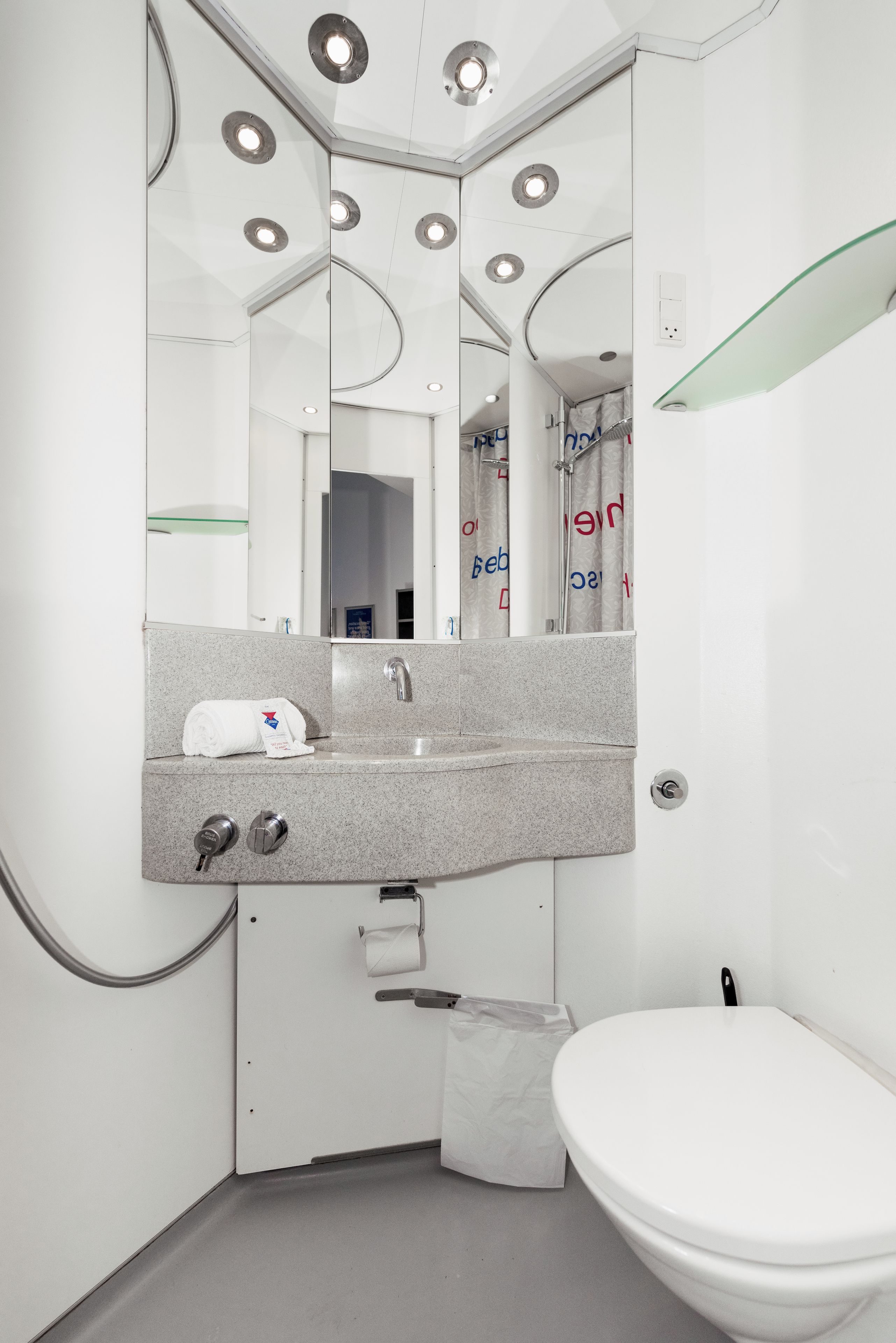 A modern bathroom with a large mirror, a sink, a toilet, and a glass shelf.