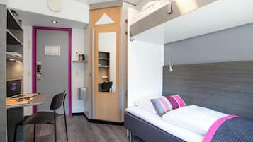 Ett kompakt hotellrum med en säng, ett skrivbord och en stol.