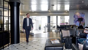 A modern lobby with a man walking, a sofa, a table with a magazine, and a large abstract painting on the wall.