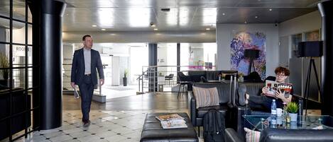 A modern lobby with a man walking, a sofa, a table with a magazine, and a large abstract painting on the wall.
