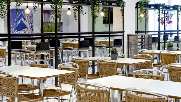 A modern cafe with wicker furniture, glass partitions, and hanging plants.