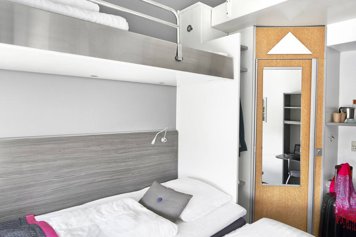 Een moderne hotelkamer met een stapelbed, een bureau met stoel en een garderobe.