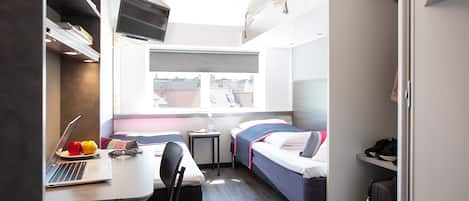 A compact room with a bed, a desk with a laptop, and a chair.