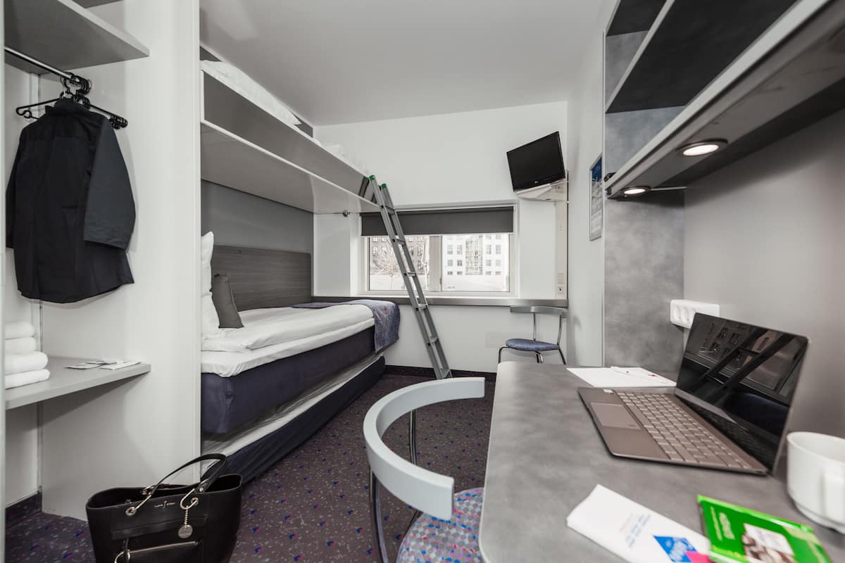 Een kleine hotelkamer met stapelbedden, een bureau met een laptop, een stoel en een tafeltje.