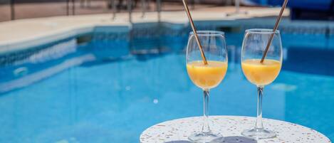 Two glasses of orange juice on a small round table by a pool.